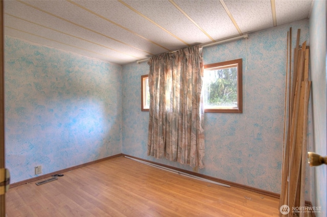 empty room featuring wallpapered walls, visible vents, and wood finished floors