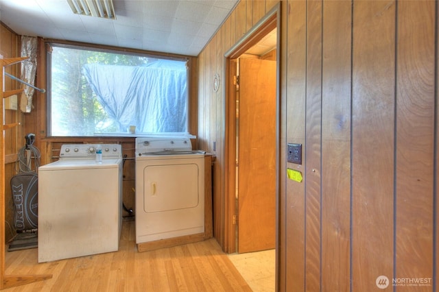 laundry area with light wood finished floors, laundry area, wood walls, and washer and clothes dryer