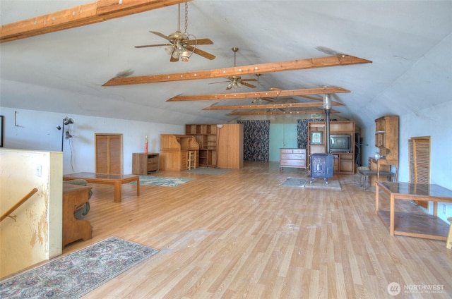 living area featuring vaulted ceiling with beams, a wood stove, a ceiling fan, and wood finished floors