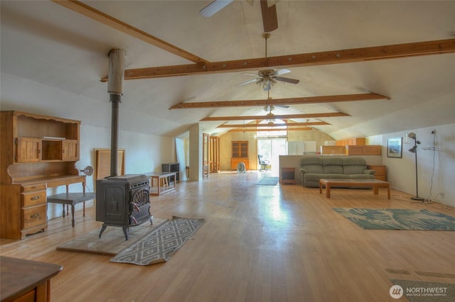 living area featuring a ceiling fan, a wood stove, vaulted ceiling with beams, and wood finished floors