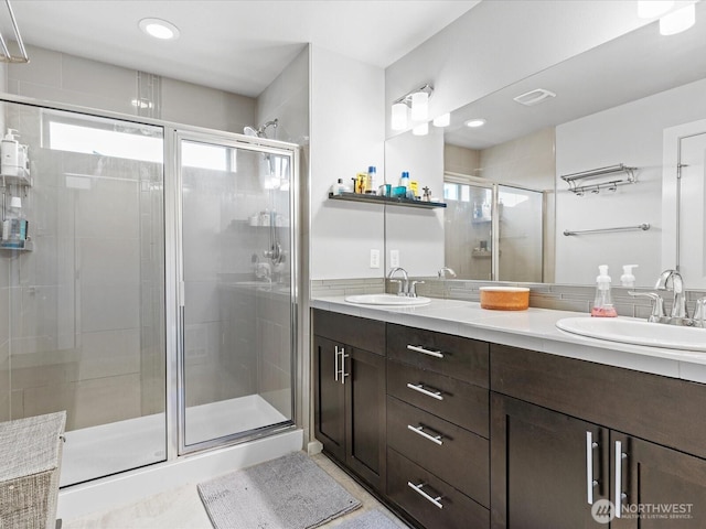 bathroom with visible vents, a sink, a shower stall, and double vanity