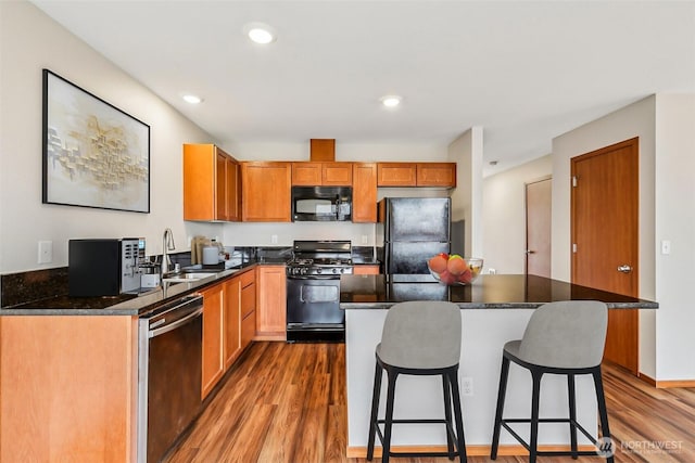 kitchen featuring wood finished floors, a kitchen island, a sink, black appliances, and a kitchen bar