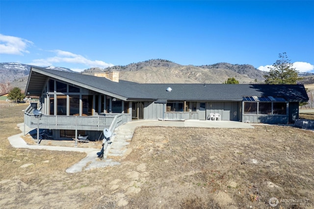 rear view of property featuring a mountain view, a chimney, a patio, and a sunroom