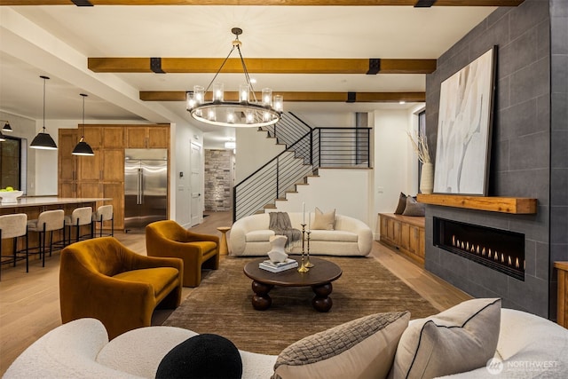 living area featuring light wood finished floors, stairway, a tiled fireplace, and beam ceiling