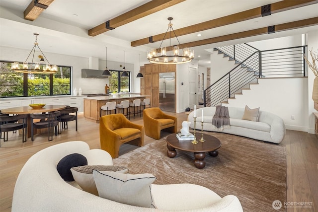 living room featuring beam ceiling, stairway, light wood-style flooring, and a notable chandelier