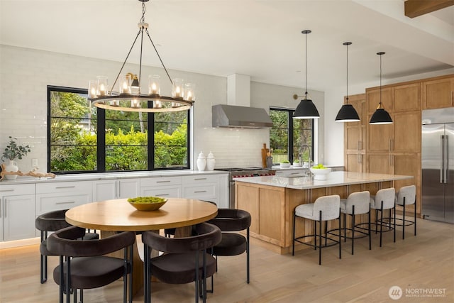 kitchen featuring wall chimney range hood, decorative backsplash, high end appliances, and light wood finished floors