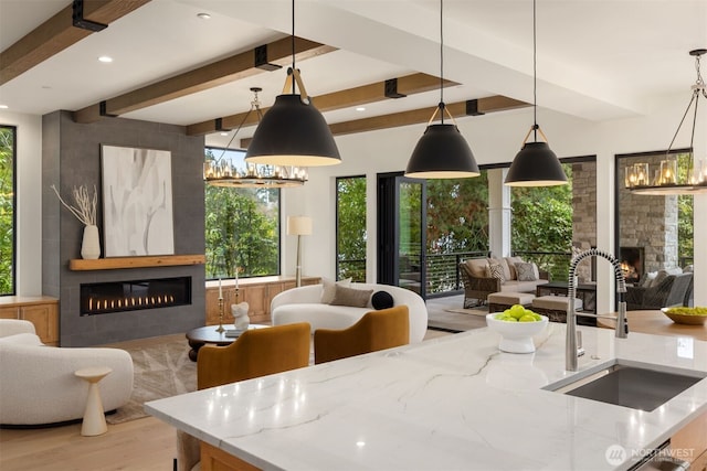 kitchen with a large fireplace, light stone counters, open floor plan, a sink, and beam ceiling