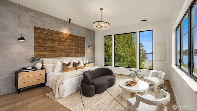 bedroom featuring wood finished floors, visible vents, baseboards, tile walls, and an inviting chandelier