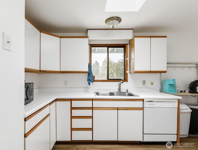 kitchen featuring black microwave, dishwasher, light countertops, white cabinetry, and a sink