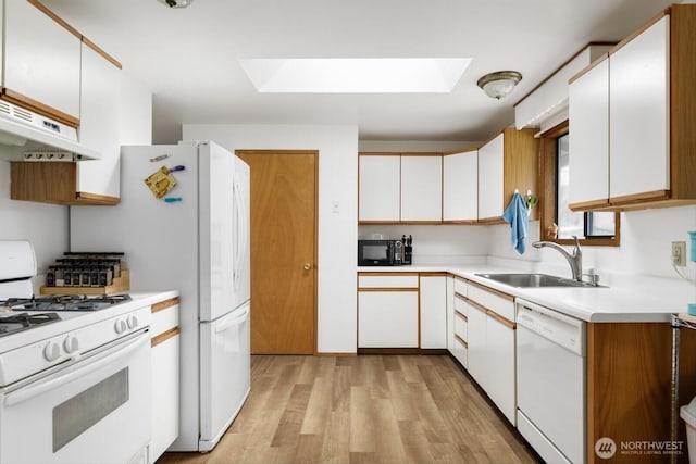 kitchen featuring a skylight, light countertops, white cabinets, a sink, and white appliances