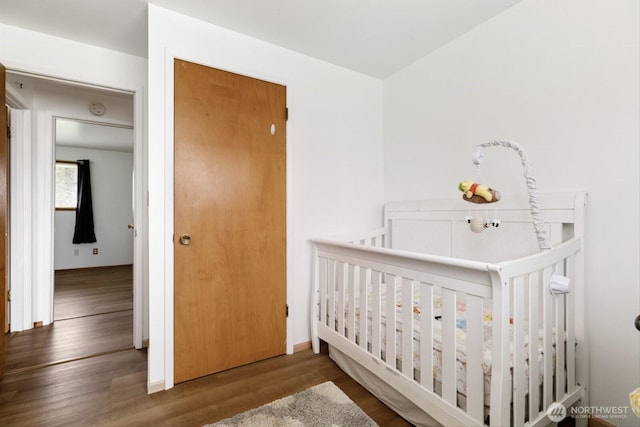 bedroom featuring a crib, baseboards, and wood finished floors