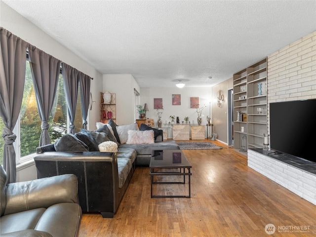 living area featuring a textured ceiling, built in shelves, a brick fireplace, and wood finished floors