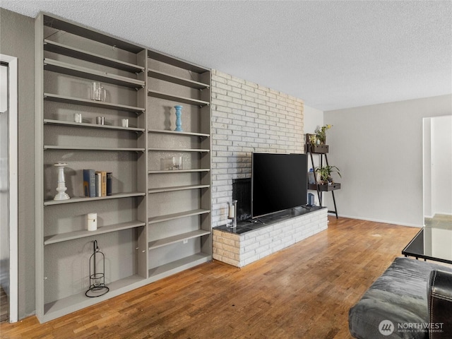 living area featuring a brick fireplace, a textured ceiling, and wood finished floors