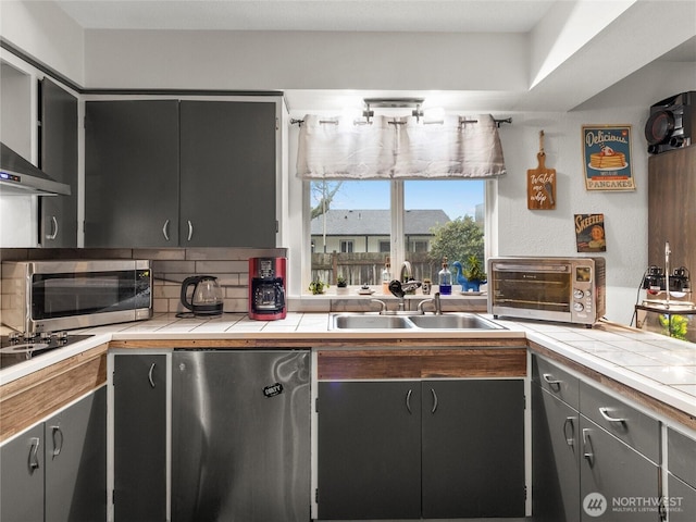 kitchen featuring a toaster, tile counters, dishwasher, stainless steel microwave, and a sink