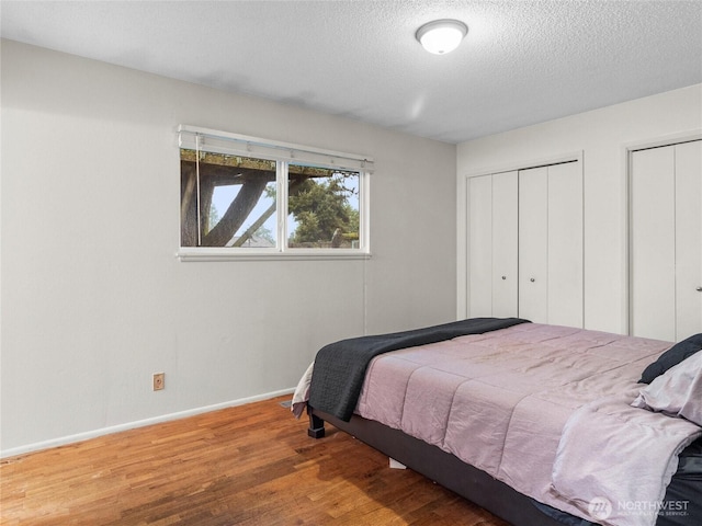 bedroom featuring multiple closets, a textured ceiling, baseboards, and wood finished floors