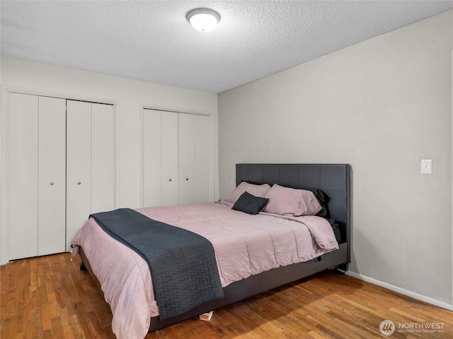 bedroom with a textured ceiling, wood finished floors, two closets, and baseboards