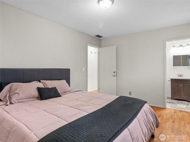 bedroom featuring visible vents, ensuite bath, a textured ceiling, light wood-type flooring, and a sink