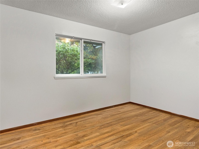 spare room with light wood-style flooring, baseboards, and a textured ceiling