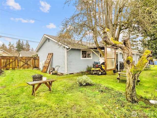 back of property featuring an outdoor fire pit, a lawn, and fence