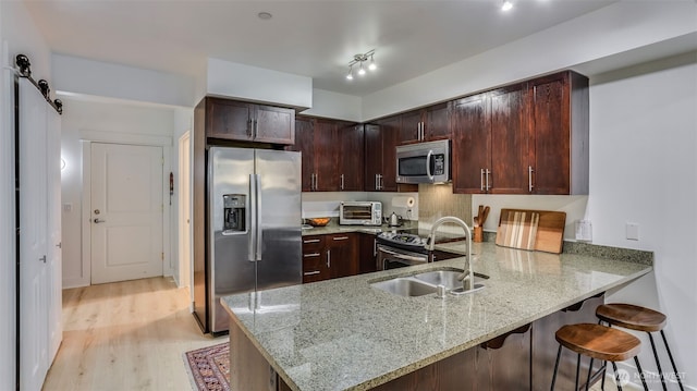 kitchen featuring stainless steel appliances, a sink, light stone countertops, a peninsula, and a kitchen breakfast bar