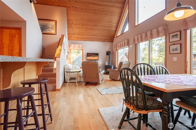 dining area featuring wooden ceiling, a wood stove, stairs, light wood-style floors, and high vaulted ceiling