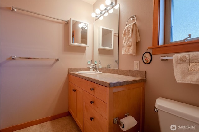 half bathroom featuring toilet, baseboards, and vanity