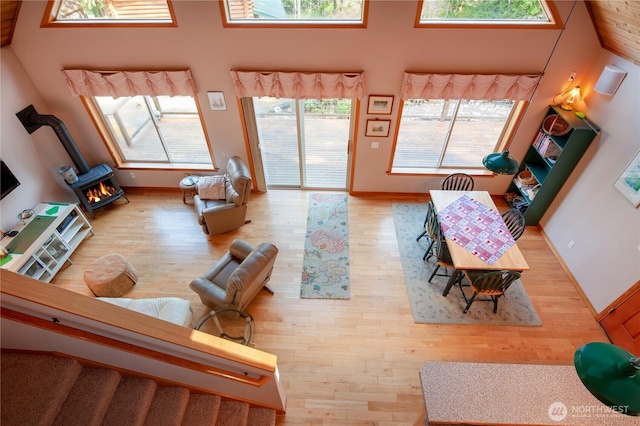 living area featuring a wood stove, a towering ceiling, baseboards, and wood finished floors