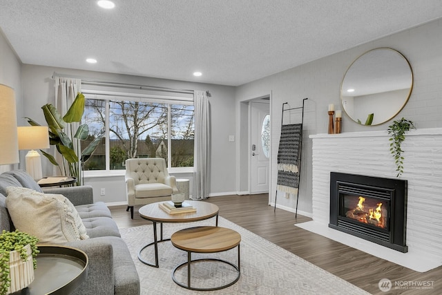 living area with dark wood-style floors, a fireplace with flush hearth, baseboards, and a textured ceiling