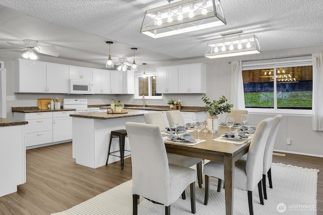 dining space with a textured ceiling, light wood-type flooring, and a ceiling fan