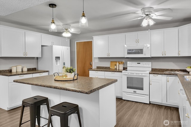 kitchen with white appliances, white cabinetry, and a center island