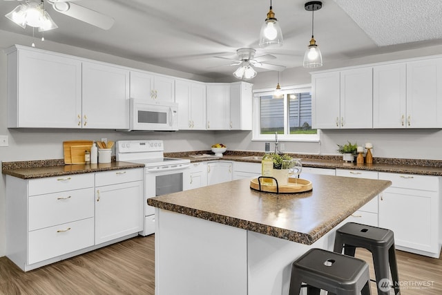 kitchen featuring a center island, a breakfast bar area, dark countertops, white cabinetry, and white appliances