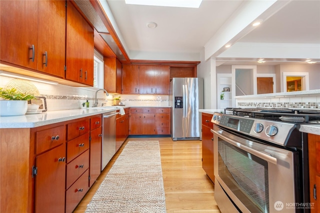 kitchen with tasteful backsplash, light wood-style flooring, stainless steel appliances, light countertops, and a sink