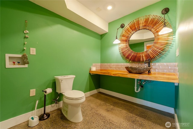 half bath with toilet, baseboards, a sink, and speckled floor