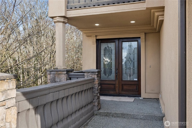 property entrance featuring french doors, a balcony, and stucco siding