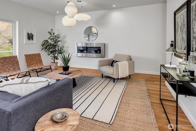 living room featuring light wood finished floors, recessed lighting, a glass covered fireplace, and baseboards