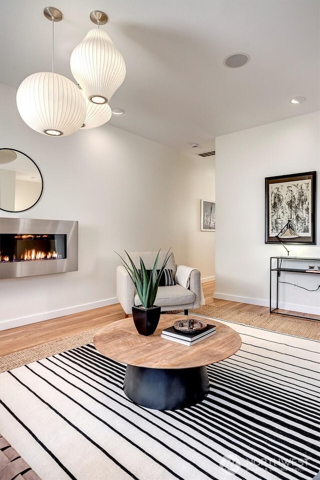 living area with a glass covered fireplace, light wood-style flooring, baseboards, and recessed lighting