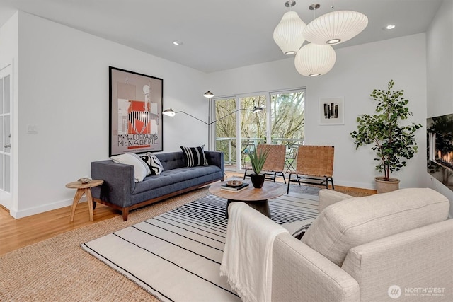 living area featuring a lit fireplace, baseboards, wood finished floors, and recessed lighting