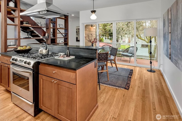 kitchen with dark countertops, brown cabinets, stainless steel gas range oven, and island range hood