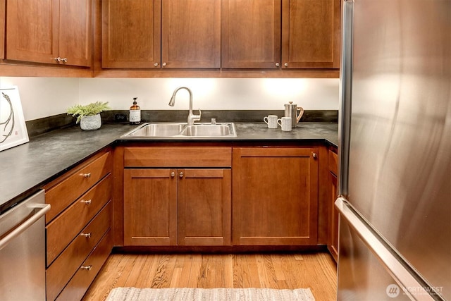 kitchen with dark countertops, light wood-style flooring, brown cabinets, stainless steel appliances, and a sink