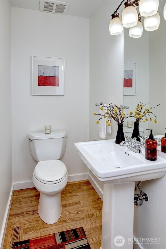 half bathroom with toilet, baseboards, visible vents, and wood finished floors