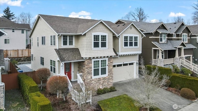 view of front of house with fence, concrete driveway, roof with shingles, stone siding, and an attached garage