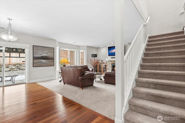 carpeted living area with hardwood / wood-style flooring, stairway, a fireplace, and baseboards