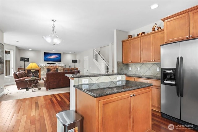 kitchen featuring tasteful backsplash, a kitchen island, stainless steel fridge with ice dispenser, open floor plan, and wood finished floors