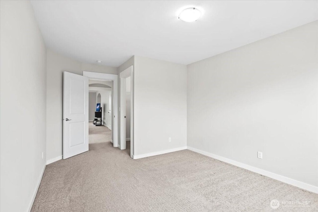 carpeted spare room with baseboards and arched walkways