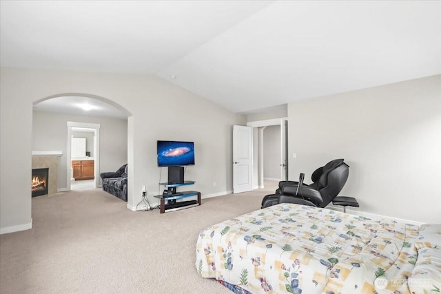 bedroom with baseboards, lofted ceiling, carpet flooring, a tile fireplace, and arched walkways