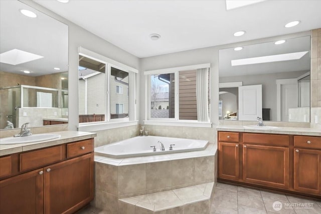 full bathroom with a bath, a stall shower, a skylight, and a sink