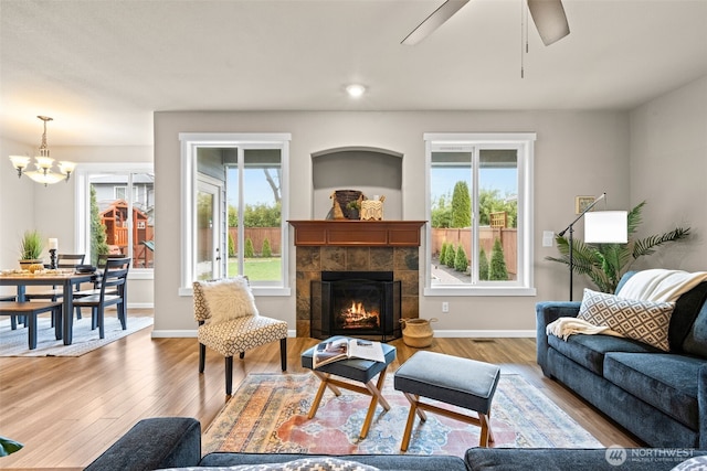 living area with ceiling fan with notable chandelier, a fireplace, baseboards, and wood finished floors