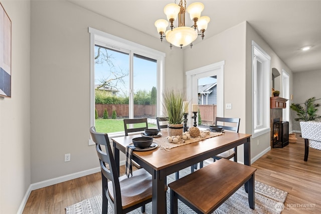 dining space with light wood-type flooring, a lit fireplace, baseboards, and a chandelier