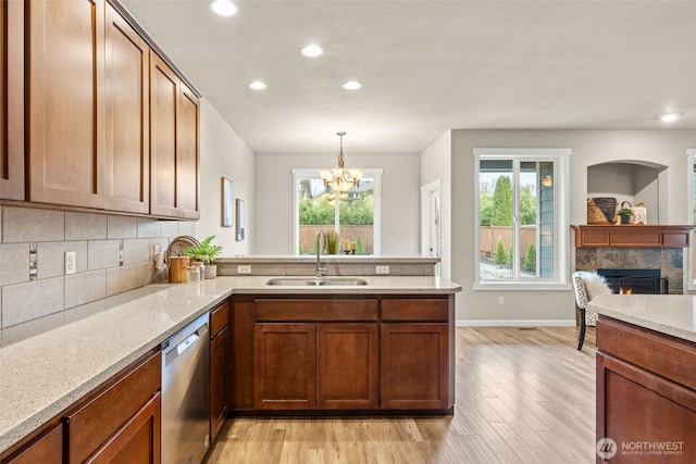 kitchen featuring tasteful backsplash, dishwasher, a peninsula, a lit fireplace, and a sink