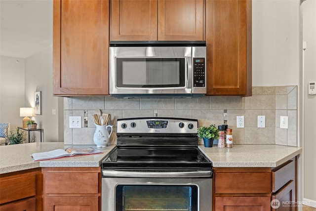 kitchen with brown cabinets, appliances with stainless steel finishes, light countertops, and backsplash